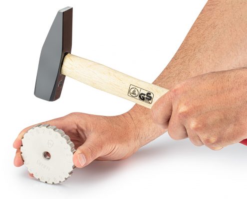 1x Pickardt Punching Wheel held by a man in his right hand. In the left hand the man holds a hammer that is ready to strike the punching wheel